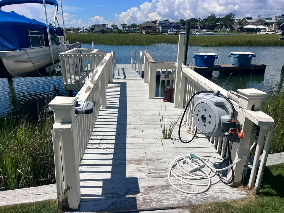 Before: weathered white wooden walkway with hose reel leading to a dock