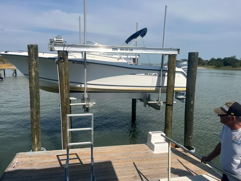 Center-console boat raised on a new boat lift beside a dock while a crew member works on the walkway
