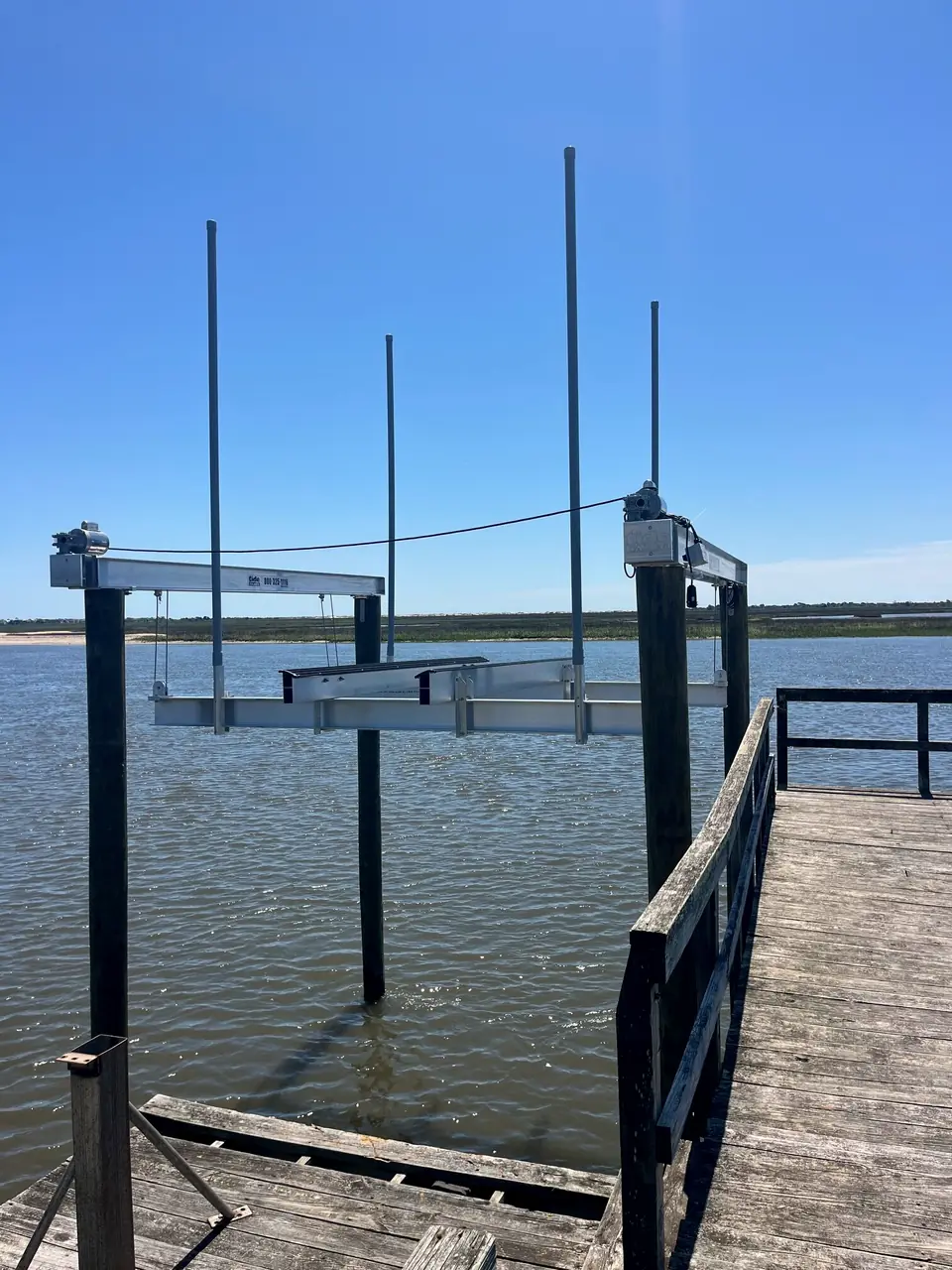 Empty boat lift cradle and pilings next to a pier on open water under blue sky
