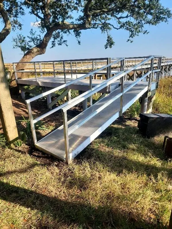 Aluminum gangway with handrails descending from a live oak bluff toward a pier