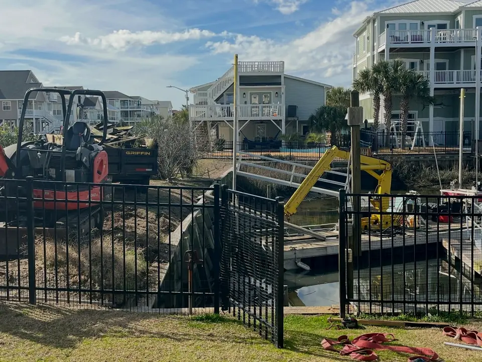 Seawall project with excavator and equipment behind a fenced canal-front yard