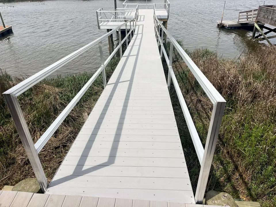 Aluminum gangway with composite decking and tall handrails crossing marsh grass
