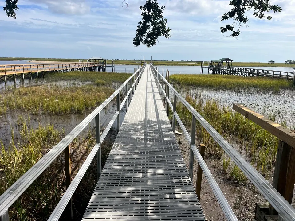 Long aluminum pier with grated decking running through marsh grass toward a covered platform