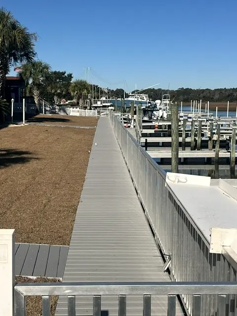 Long aluminum pier with railings running past a marina of boat slips