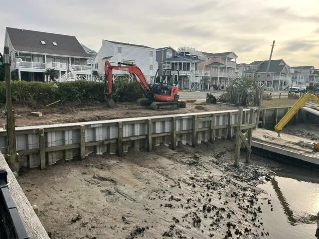 Mini excavator setting vinyl seawall panels along a canal lot