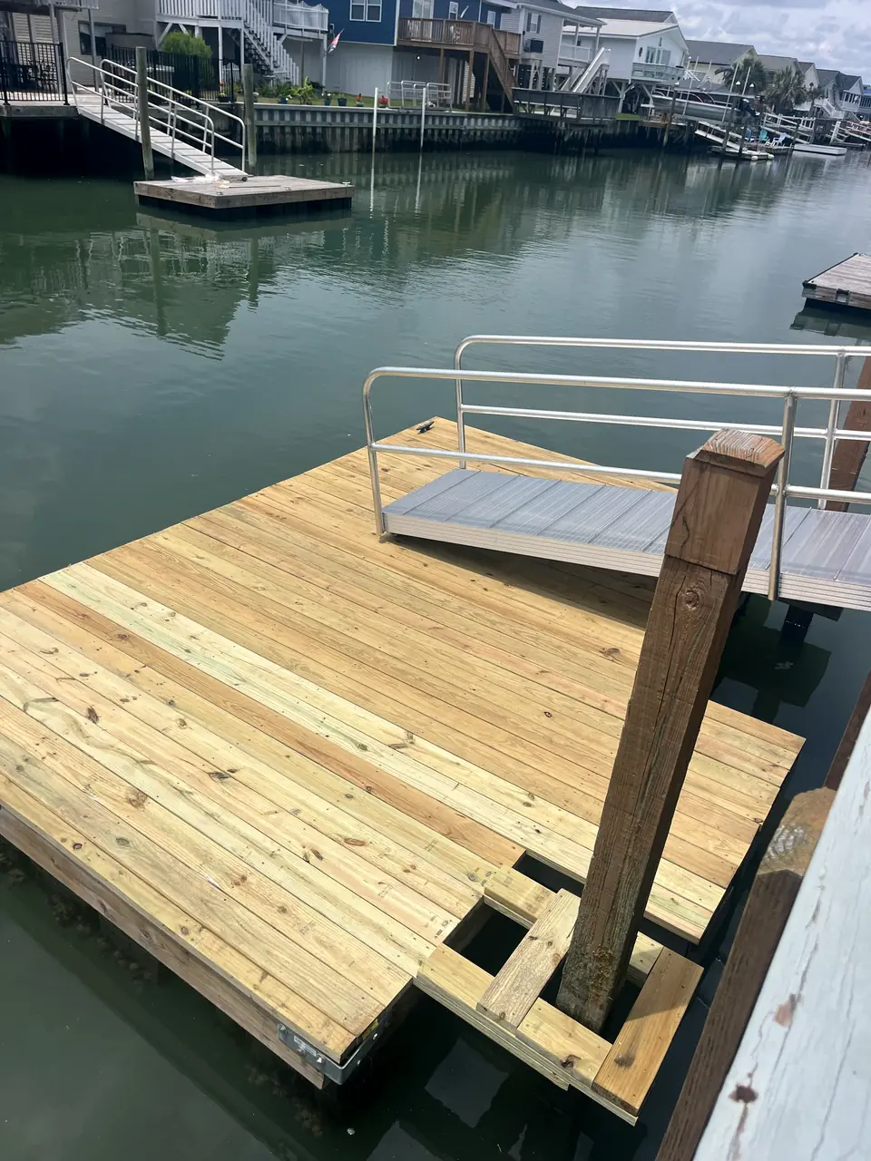 New pressure-treated wood floating dock with a piling guide beside an aluminum gangway